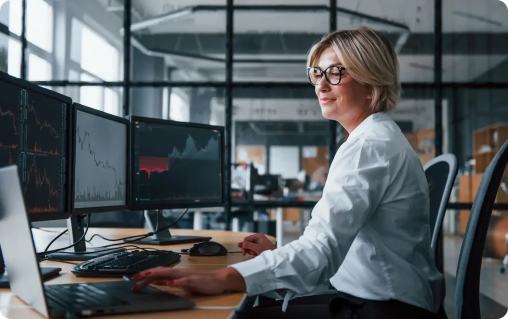 A woman works a desk with multiple external monitors.